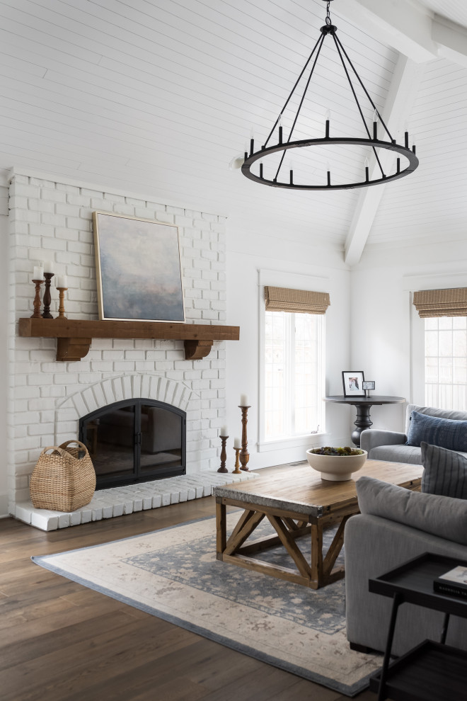 Inspiration for a large country l-shaped medium tone wood floor, brown floor, shiplap ceiling and vaulted ceiling living room remodel in Chicago with a farmhouse sink, shaker cabinets, white cabinets, quartz countertops, white backsplash, window backsplash, stainless steel appliances, an island, white countertops, white walls, a standard fireplace and a brick fireplace
