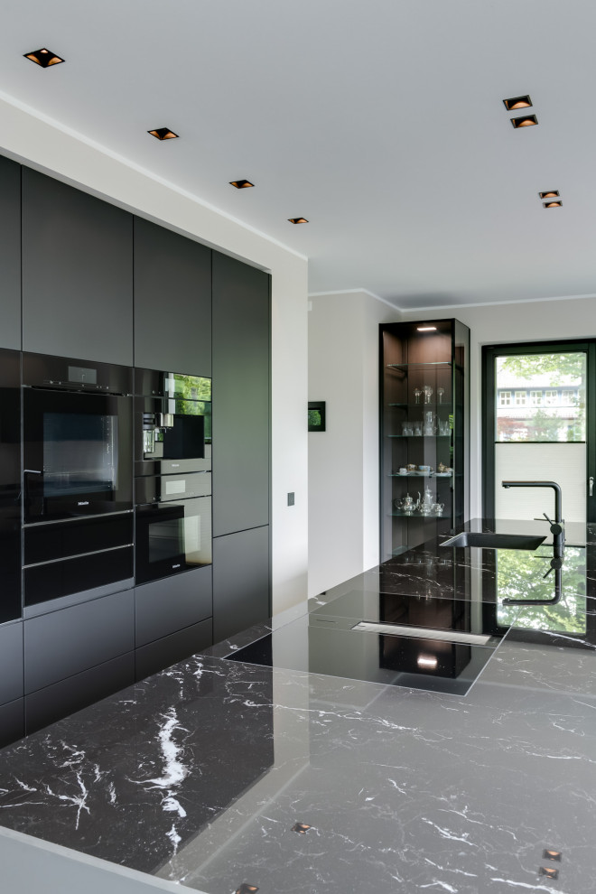 Design ideas for an expansive modern galley open plan kitchen in Hamburg with an integrated sink, flat-panel cabinets, black cabinets, quartz benchtops, black splashback, ceramic splashback, black appliances, ceramic floors, with island, grey floor, black benchtop and recessed.