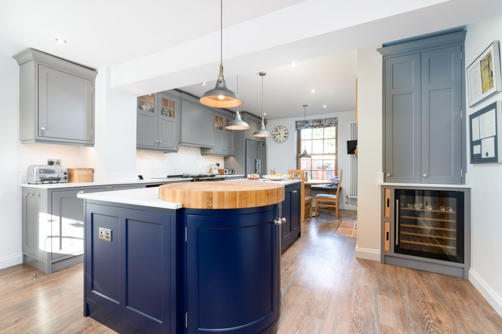 This is an example of a large traditional eat-in kitchen in Other with an integrated sink, shaker cabinets, solid surface benchtops, white splashback, black appliances, medium hardwood floors, with island and white benchtop.