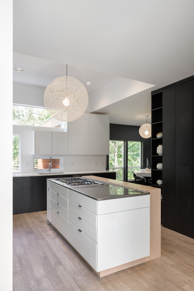 Design ideas for a contemporary kitchen in Portland with an undermount sink, flat-panel cabinets, black cabinets, stainless steel benchtops, white splashback, window splashback, panelled appliances, light hardwood floors, with island and beige floor.