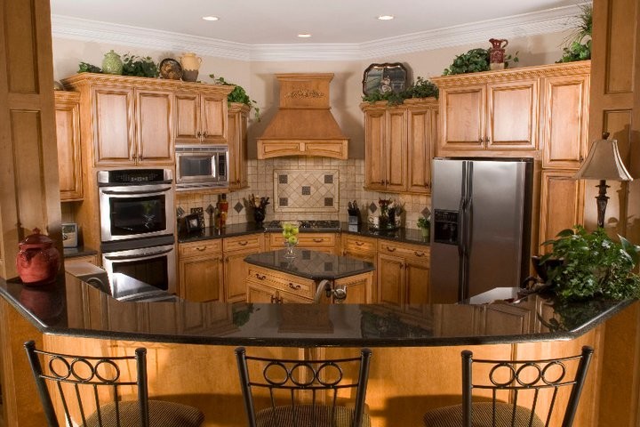 Photo of a mid-sized traditional l-shaped eat-in kitchen in Raleigh with light wood cabinets, stainless steel appliances, with island, raised-panel cabinets, quartz benchtops, beige splashback, travertine splashback and black benchtop.