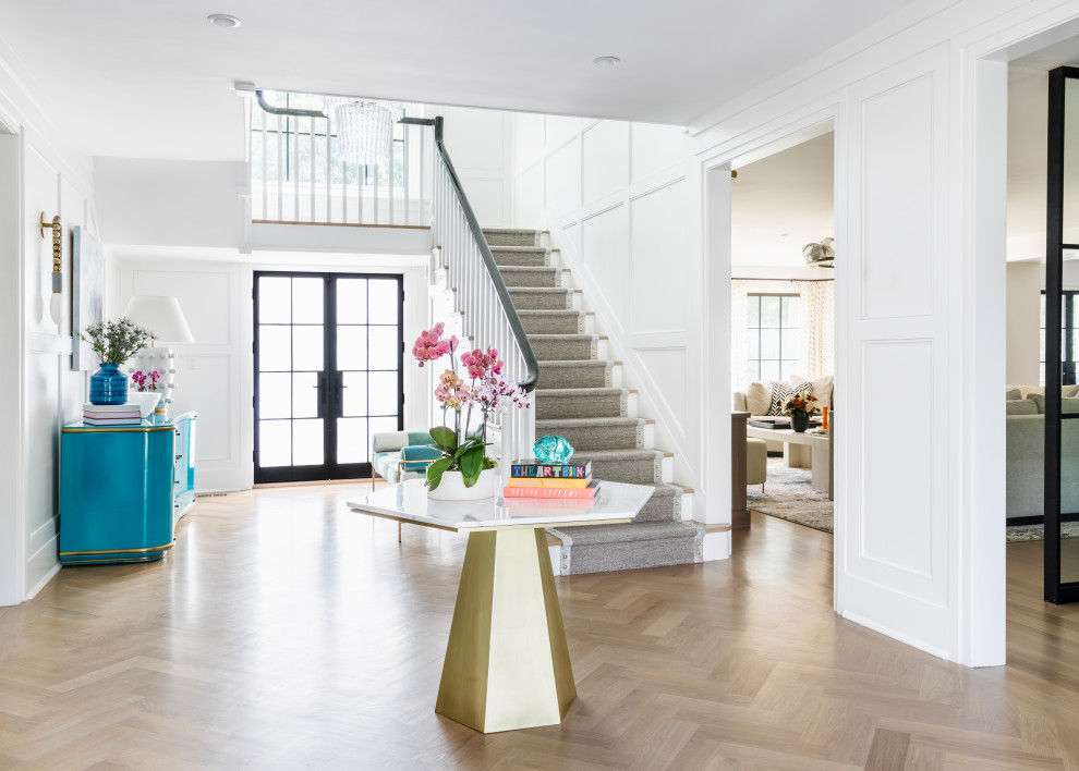 This is an example of a contemporary foyer in New York with white walls, medium hardwood floors, a double front door, a glass front door, brown floor and panelled walls.