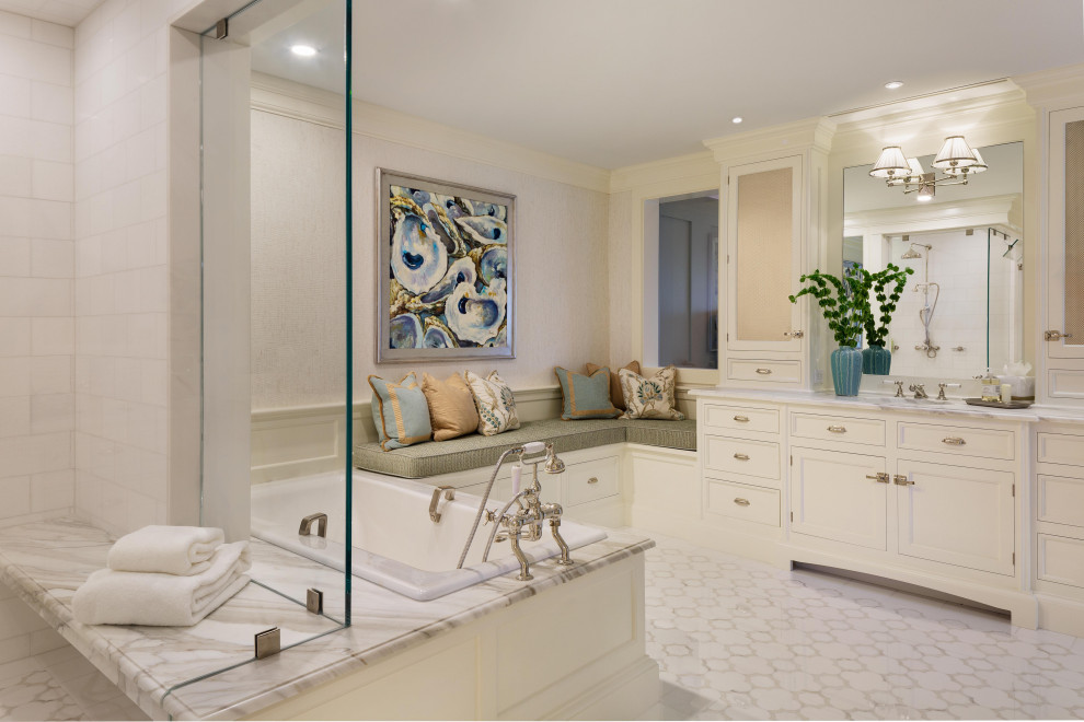 Photo of a large beach style master bathroom in Miami with recessed-panel cabinets, white cabinets, a drop-in tub, an alcove shower, beige walls, ceramic floors, marble benchtops, white floor, a hinged shower door and grey benchtops.