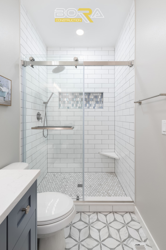 На фото: маленькая ванная комната в стиле неоклассика (современная классика) с фасадами в стиле шейкер, синими фасадами, душем над ванной, раздельным унитазом, белой плиткой, керамической плиткой, белыми стенами, душевой кабиной, врезной раковиной, столешницей из искусственного кварца, душем с раздвижными дверями, белой столешницей, тумбой под одну раковину и напольной тумбой для на участке и в саду