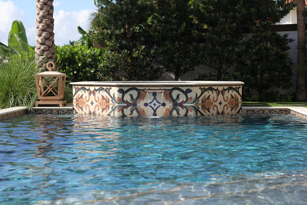 Photo of a mid-sized contemporary backyard custom-shaped pool in Miami with a water feature and natural stone pavers.
