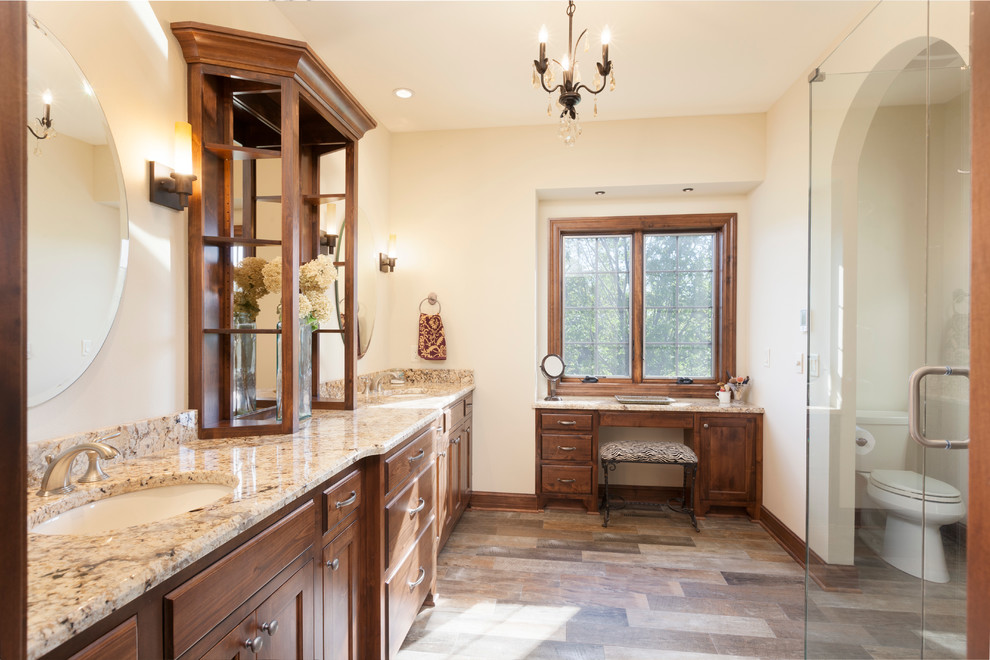 This is an example of a mid-sized traditional master bathroom in Milwaukee with flat-panel cabinets, medium wood cabinets, a corner shower, a two-piece toilet, brown tile, ceramic tile, beige walls, ceramic floors, an undermount sink and granite benchtops.