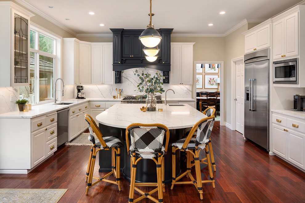 Inspiration for a traditional u-shaped kitchen in Seattle with an undermount sink, raised-panel cabinets, white cabinets, white splashback, stainless steel appliances, medium hardwood floors, with island, red floor and white benchtop.