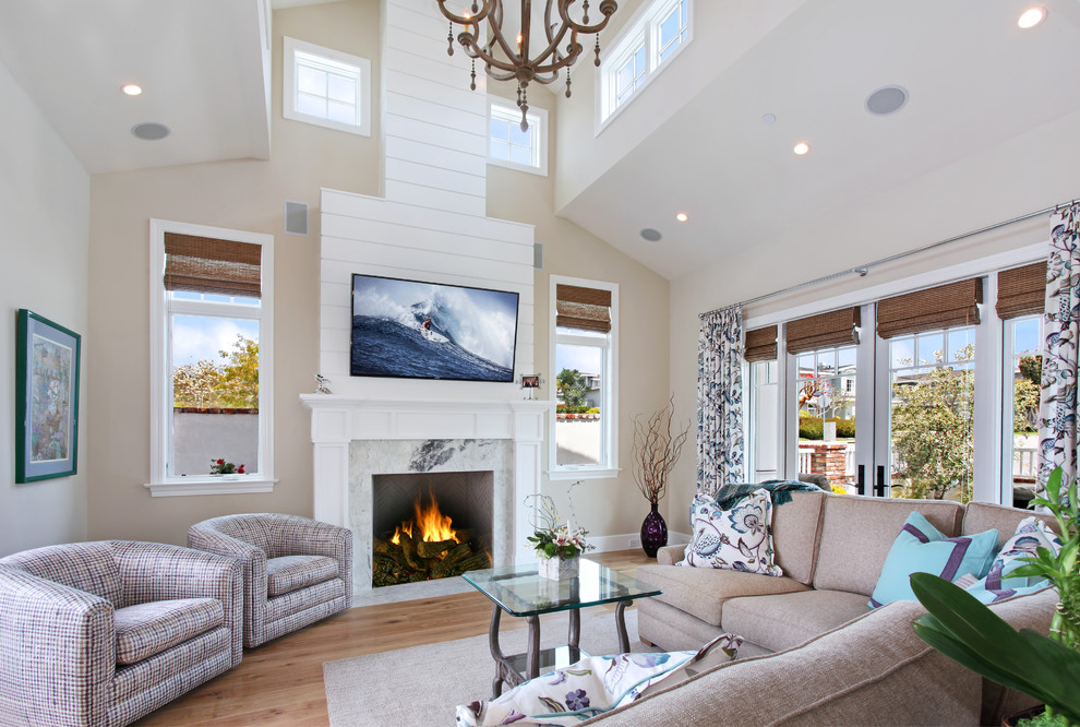This is an example of a beach style living room with beige walls, medium hardwood floors, a standard fireplace, a stone fireplace surround and a wall-mounted tv.