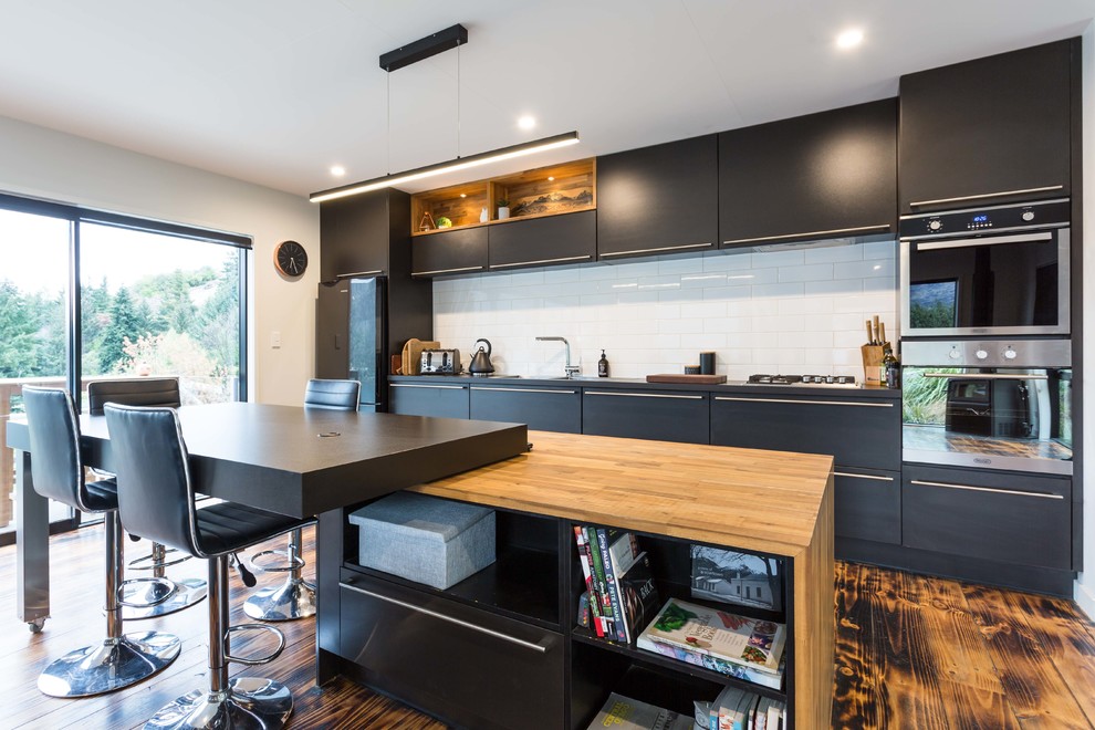 Photo of a contemporary single-wall eat-in kitchen in Other with flat-panel cabinets, black cabinets, white splashback, subway tile splashback, stainless steel appliances, medium hardwood floors and with island.