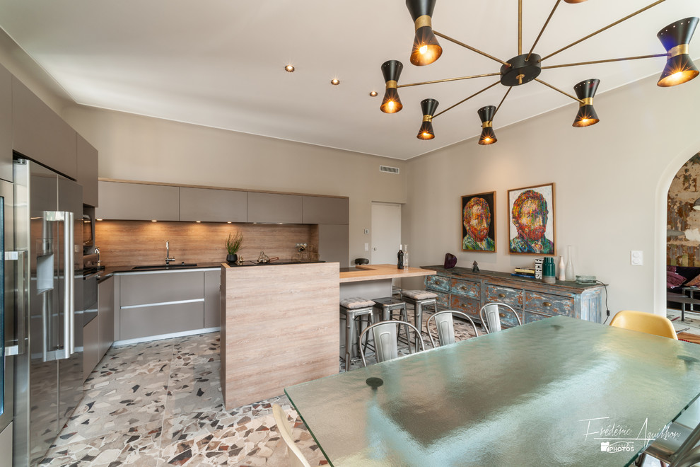 Inspiration pour cuisine américaine en U avec un évier encastré, un placard à porte affleurante, des portes de placard grises, un plan de travail en quartz modifié, une crédence marron, une crédence en bois, un électroménager en acier inoxydable, carreaux de ciment au sol, îlot, un sol multicolore et plan de travail noir.