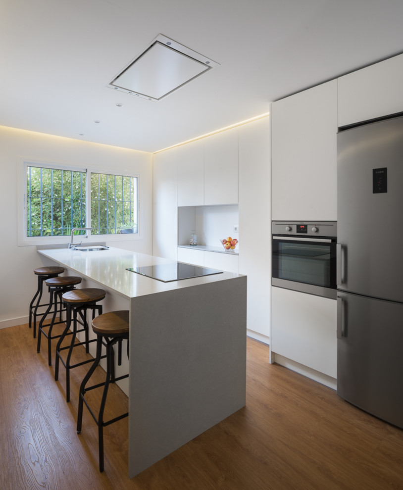 Mid-sized contemporary galley kitchen in Seville with an undermount sink, flat-panel cabinets, white cabinets, white splashback, with island, brown floor and white benchtop.