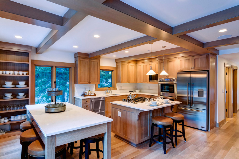 This is an example of a mid-sized country l-shaped open plan kitchen in Portland with an undermount sink, shaker cabinets, quartzite benchtops, white splashback, stainless steel appliances, multiple islands, white benchtop, medium wood cabinets, medium hardwood floors and brown floor.