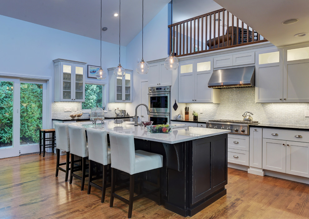 This is an example of a mid-sized contemporary l-shaped eat-in kitchen in New York with a farmhouse sink, shaker cabinets, white cabinets, quartzite benchtops, grey splashback, glass tile splashback, stainless steel appliances, medium hardwood floors, with island and brown floor.