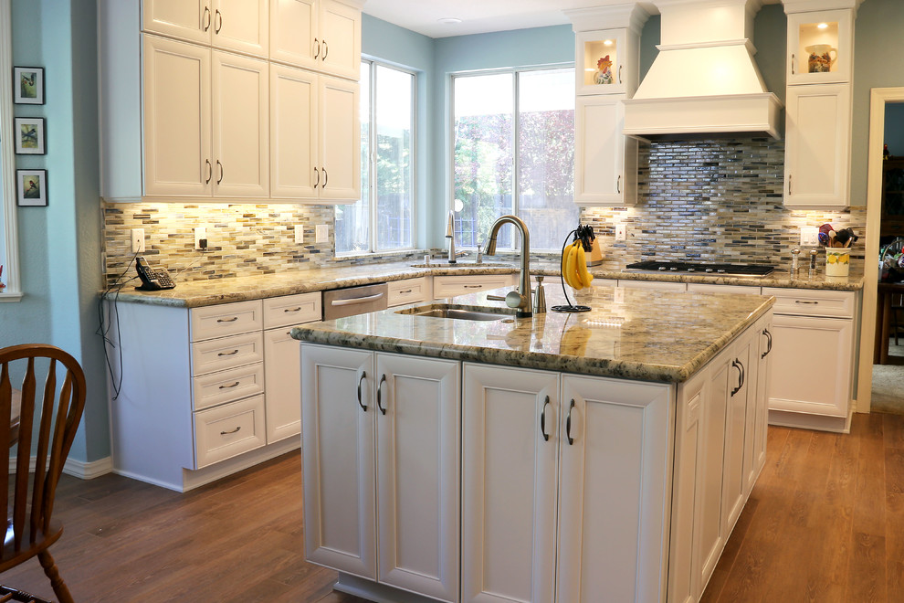 Photo of a beach style l-shaped eat-in kitchen in Sacramento with an undermount sink, flat-panel cabinets, white cabinets, granite benchtops, multi-coloured splashback, glass tile splashback, stainless steel appliances, porcelain floors and with island.