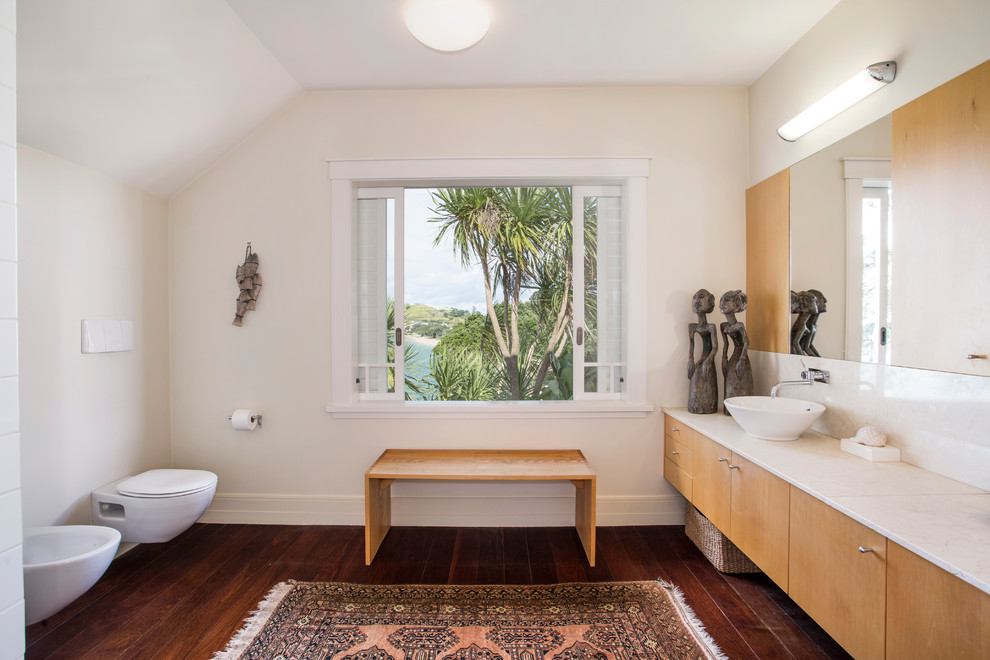 Photo of a contemporary bathroom in Auckland with flat-panel cabinets, medium wood cabinets, a wall-mount toilet, white walls, dark hardwood floors and a vessel sink.