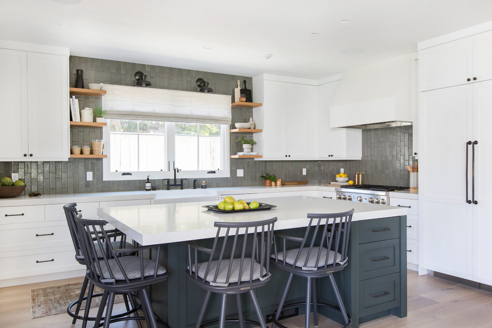 Inspiration for a mid-sized transitional l-shaped kitchen in San Diego with a farmhouse sink, shaker cabinets, white cabinets, grey splashback, subway tile splashback, panelled appliances, light hardwood floors, with island, solid surface benchtops and beige floor.