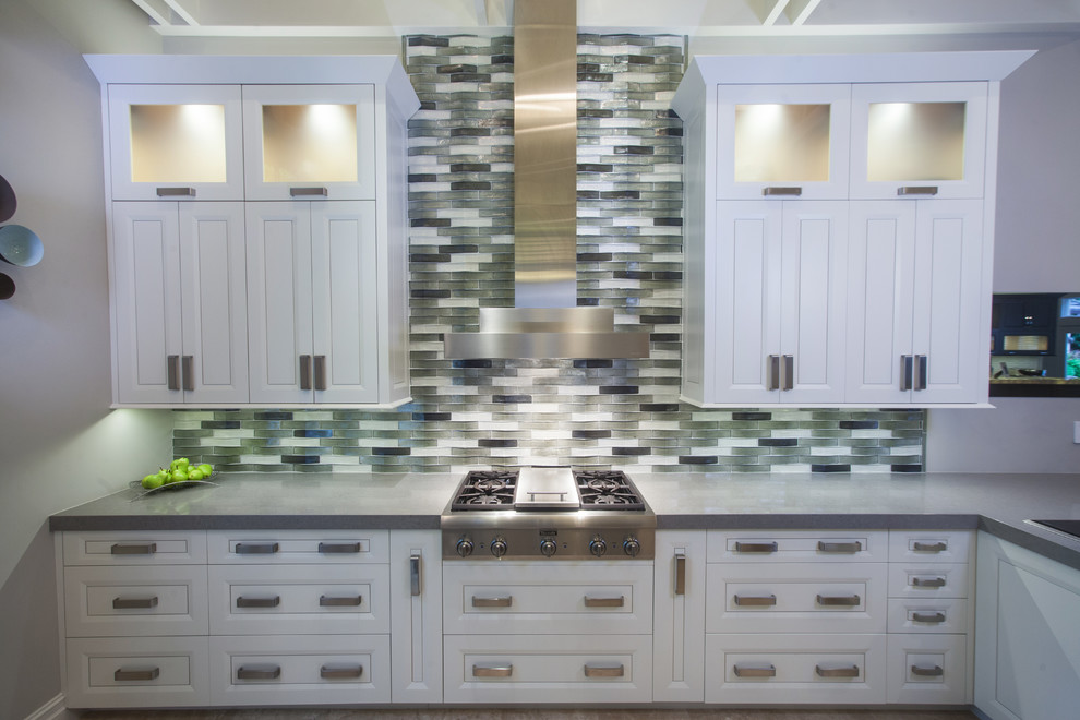 Example of a large transitional u-shaped porcelain tile and beige floor kitchen design with raised-panel cabinets, white cabinets, gray backsplash, glass tile backsplash, stainless steel appliances, an island, an undermount sink and solid surface countertops