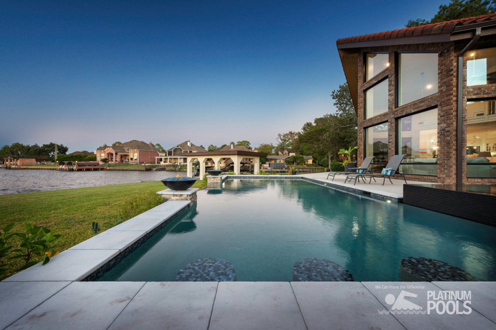 Large contemporary back rectangular infinity swimming pool in Houston with concrete paving.