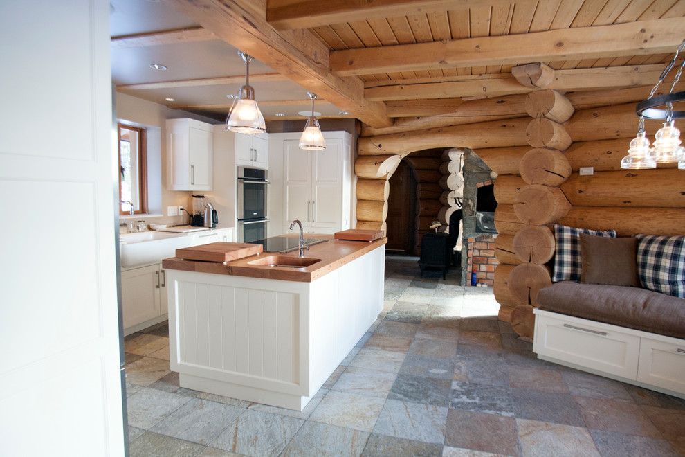 This is an example of a large country u-shaped eat-in kitchen in Vancouver with a farmhouse sink, shaker cabinets, white cabinets, wood benchtops, stainless steel appliances, slate floors and with island.