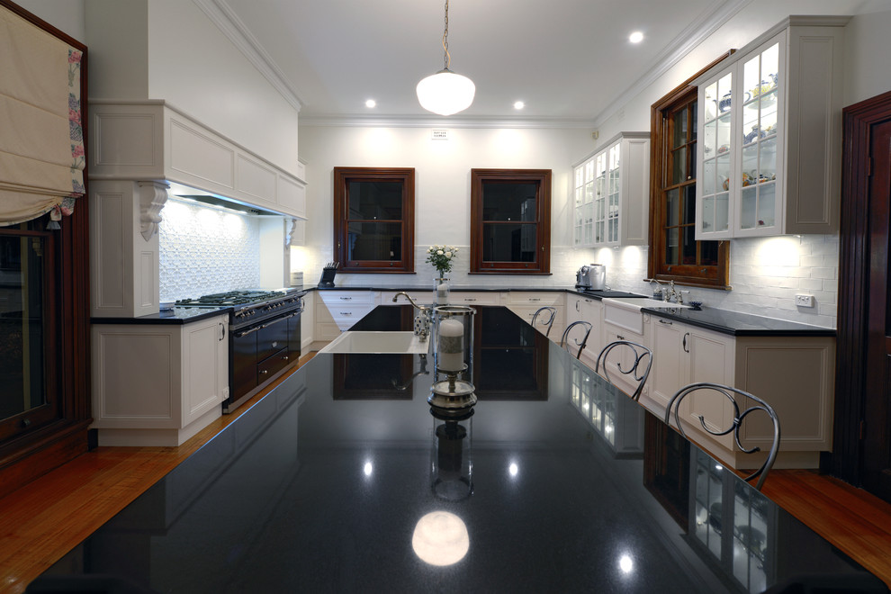 Design ideas for an expansive traditional u-shaped eat-in kitchen in Newcastle - Maitland with a farmhouse sink, recessed-panel cabinets, white cabinets, granite benchtops, white splashback, subway tile splashback, medium hardwood floors and with island.