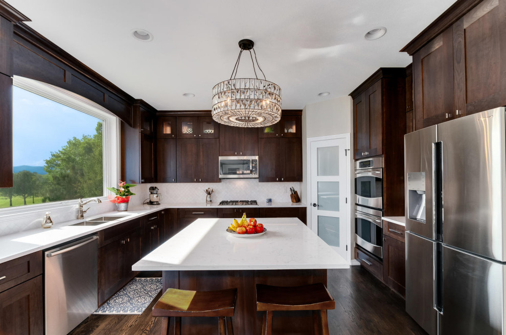 Inspiration for a mid-sized transitional kitchen in Denver with a double-bowl sink, shaker cabinets, brown cabinets, quartz benchtops, white splashback, marble splashback, stainless steel appliances, dark hardwood floors, with island, brown floor and white benchtop.