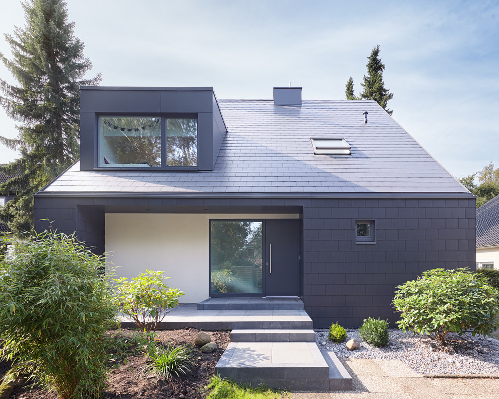 This is an example of a contemporary one-storey black house exterior in Hamburg with concrete fiberboard siding, a gable roof and a shingle roof.
