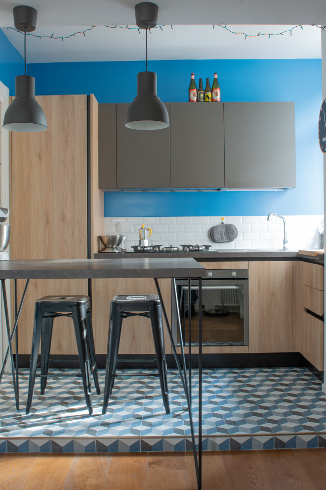 This is an example of a small contemporary l-shaped eat-in kitchen in Rome with a single-bowl sink, light wood cabinets, laminate benchtops, white splashback, porcelain splashback, stainless steel appliances, porcelain floors, a peninsula, blue floor, grey benchtop and flat-panel cabinets.