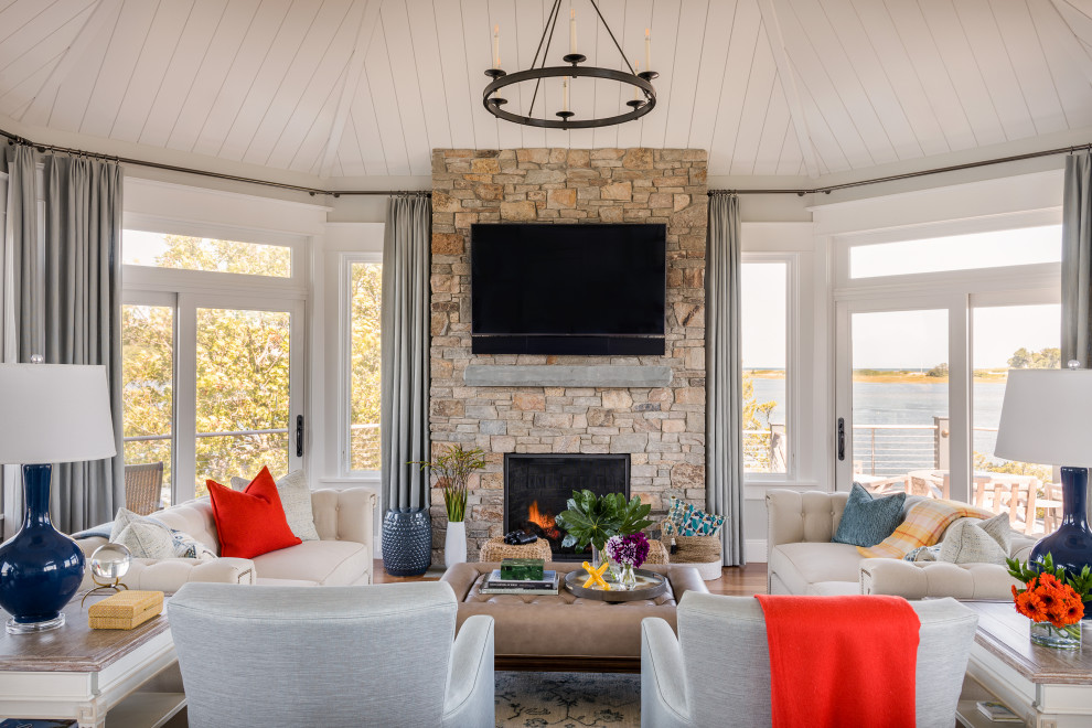Beach style living room in Boston with grey walls, medium hardwood floors, a standard fireplace, a stone fireplace surround, a wall-mounted tv and timber.