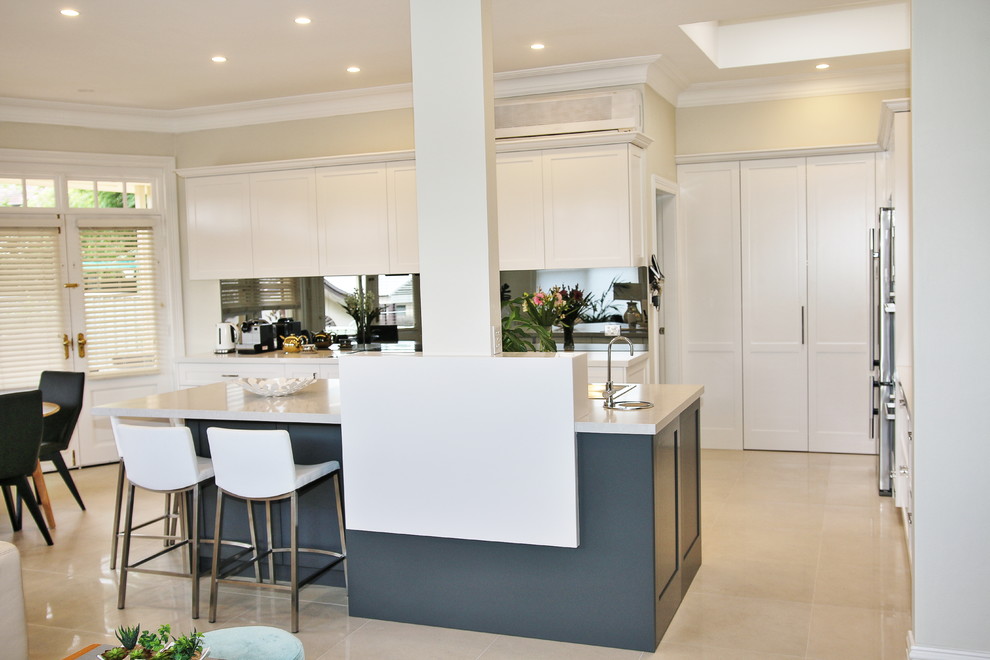 Photo of a large transitional l-shaped eat-in kitchen in Sydney with a drop-in sink, shaker cabinets, white cabinets, quartz benchtops, grey splashback, glass sheet splashback, stainless steel appliances, ceramic floors and with island.