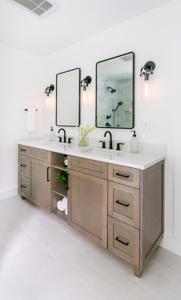 This is an example of a mid-sized transitional master bathroom in Baltimore with furniture-like cabinets, medium wood cabinets, a freestanding tub, a corner shower, a two-piece toilet, white tile, marble, white walls, ceramic floors, an undermount sink, engineered quartz benchtops, white floor, a hinged shower door, white benchtops, a niche, a double vanity and a freestanding vanity.