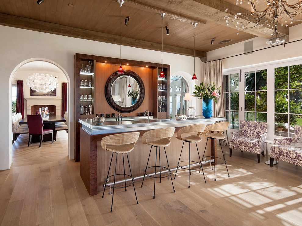 This is an example of a mediterranean galley seated home bar in Santa Barbara with open cabinets, light hardwood floors and dark wood cabinets.