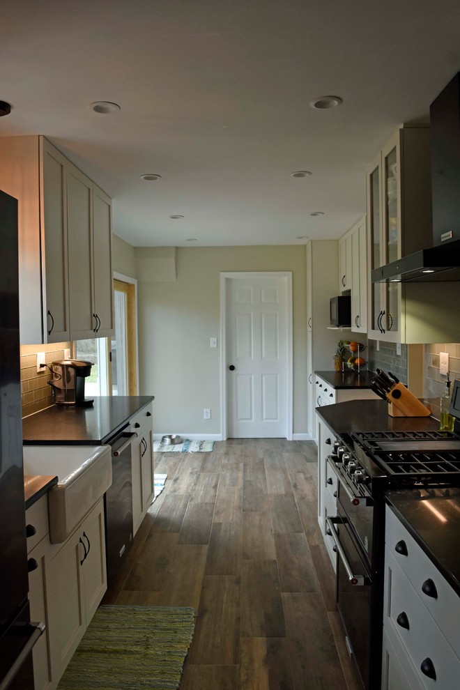 Enclosed kitchen - mid-sized transitional galley laminate floor and brown floor enclosed kitchen idea in DC Metro with a farmhouse sink, shaker cabinets, white cabinets, granite countertops, gray backsplash, subway tile backsplash, stainless steel appliances, no island and black countertops