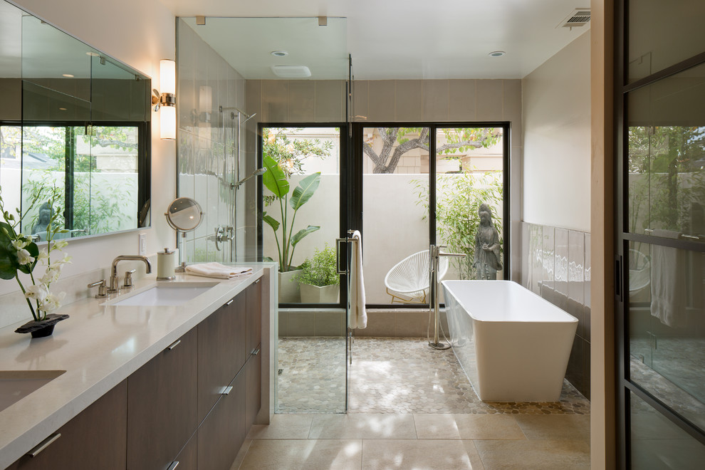 Design ideas for a mid-sized contemporary master bathroom in San Diego with flat-panel cabinets, dark wood cabinets, a freestanding tub, a curbless shower, an undermount sink, beige floor, gray tile, beige walls, pebble tile floors, a hinged shower door and white benchtops.