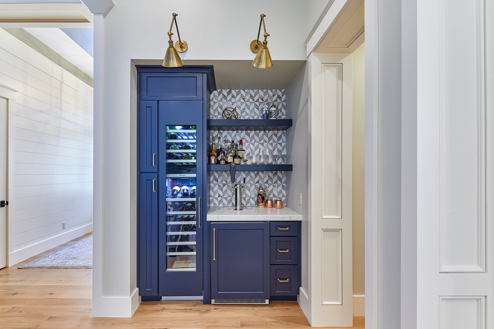 This is an example of a large arts and crafts single-wall home bar in Charleston with blue cabinets, grey splashback, mosaic tile splashback, light hardwood floors, brown floor and white benchtop.