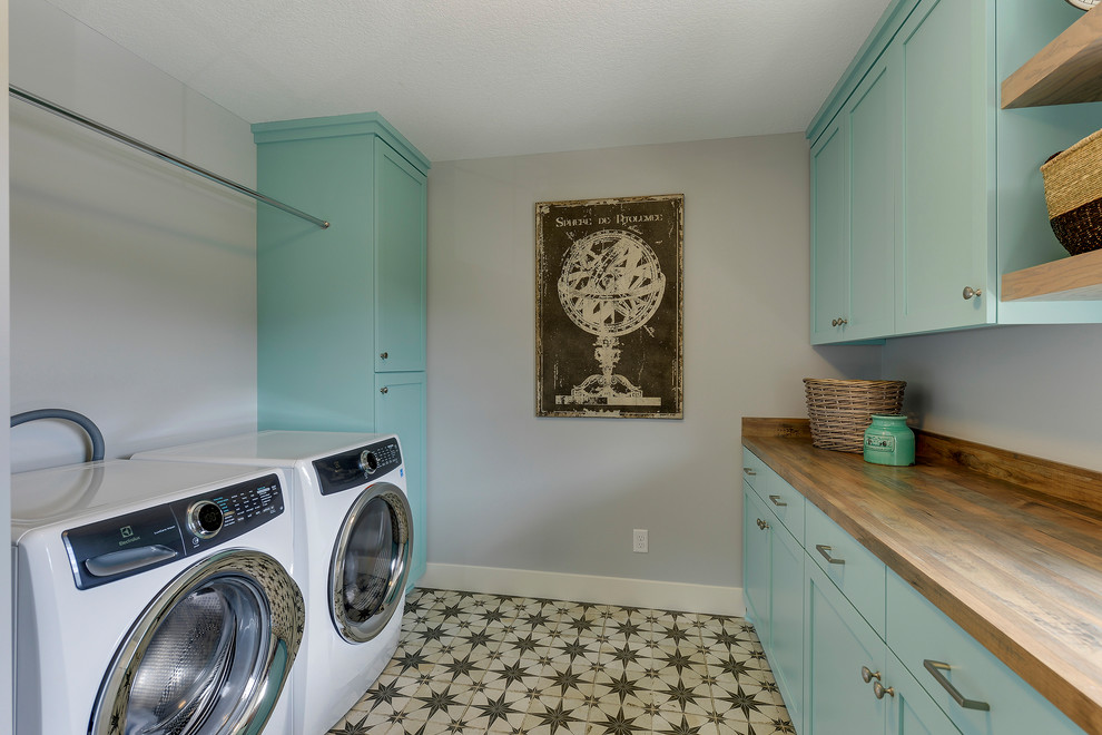 Inspiration for a mid-sized country galley utility room in Minneapolis with a drop-in sink, shaker cabinets, turquoise cabinets, laminate benchtops, grey walls, ceramic floors, a side-by-side washer and dryer, multi-coloured floor and brown benchtop.