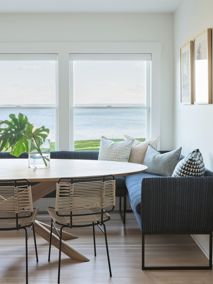 Inspiration for a medium sized beach style dining room in New York with banquette seating, white walls, light hardwood flooring, a standard fireplace, a brick fireplace surround and brown floors.