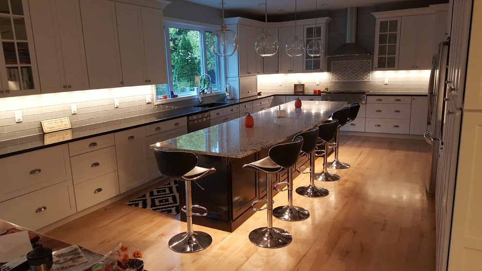 Example of a mid-sized transitional single-wall light wood floor and yellow floor eat-in kitchen design with an undermount sink, shaker cabinets, white cabinets, quartz countertops, gray backsplash, glass tile backsplash, stainless steel appliances and an island