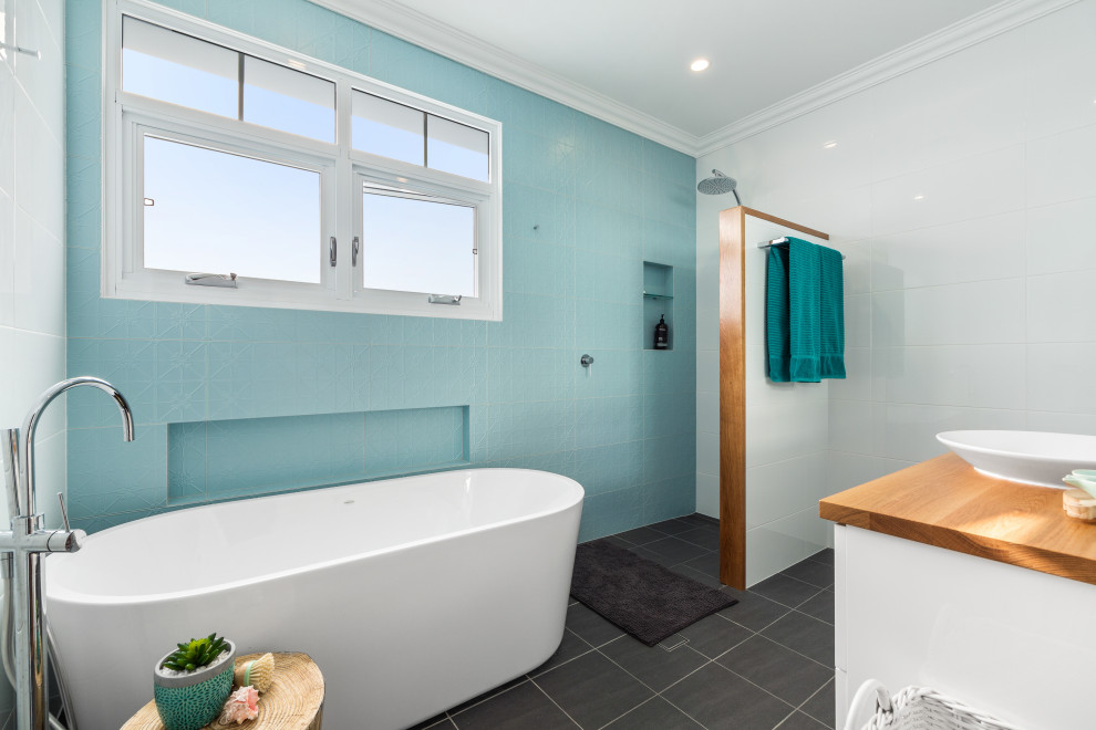 Inspiration for a beach style bathroom in Central Coast with white cabinets, a freestanding tub, a curbless shower, blue tile, a vessel sink, wood benchtops, grey floor, an open shower, brown benchtops and a single vanity.