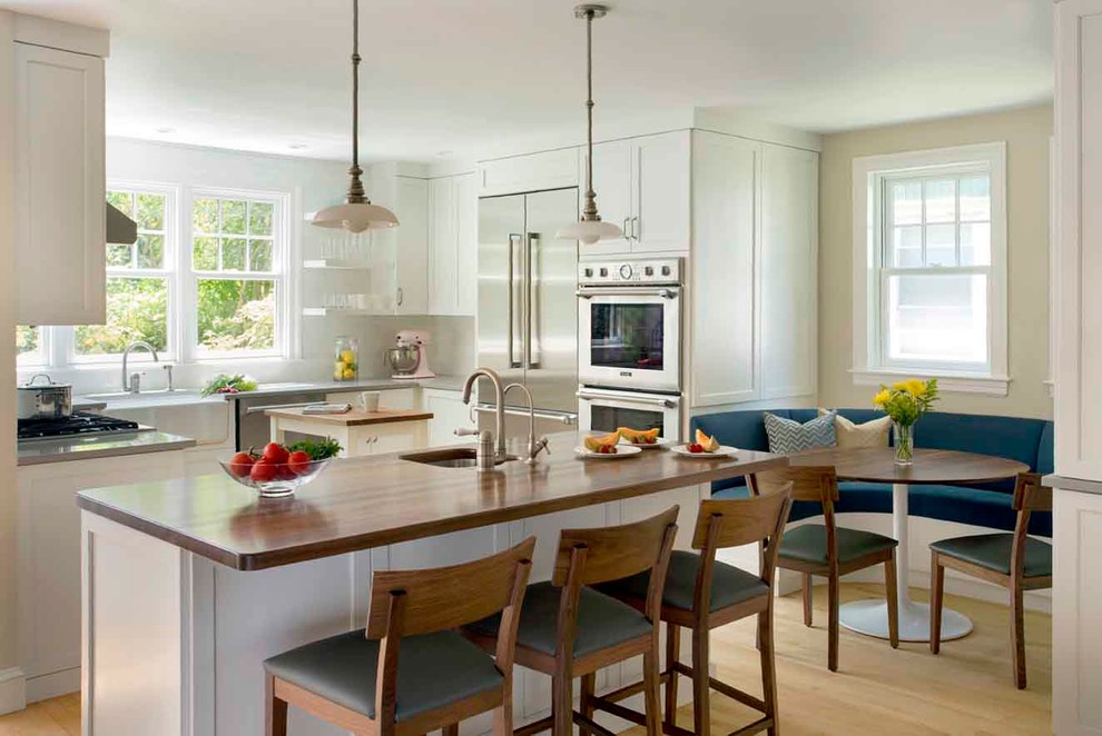 This is an example of a mid-sized traditional u-shaped eat-in kitchen in Boston with a farmhouse sink, shaker cabinets, white cabinets, quartz benchtops, white splashback, stone tile splashback, stainless steel appliances, light hardwood floors, with island, brown floor and grey benchtop.