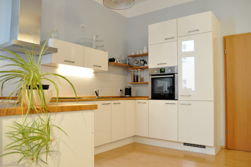 Diseño de cocina contemporánea pequeña sin isla con puertas de armario blancas, encimera de madera, salpicadero verde, suelo laminado y suelo marrón