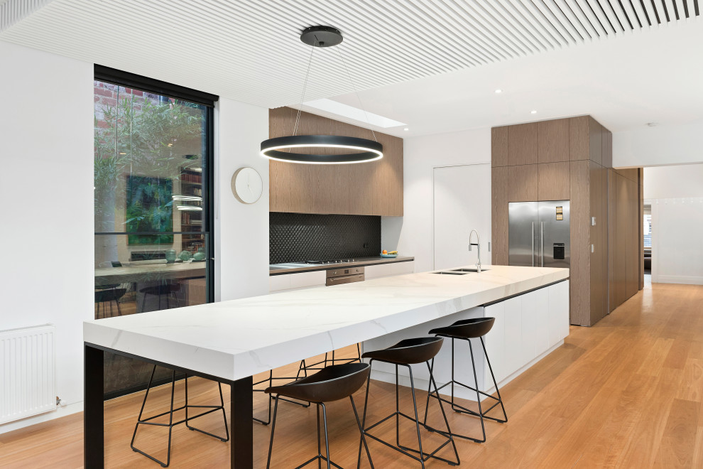 Design ideas for a contemporary u-shaped kitchen in Melbourne with an undermount sink, flat-panel cabinets, medium wood cabinets, black splashback, stainless steel appliances, medium hardwood floors, with island, brown floor and grey benchtop.