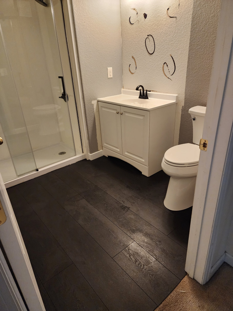 Inspiration for a small contemporary 3/4 bathroom in Denver with a two-piece toilet, vinyl floors, black floor, a sliding shower screen, white benchtops, an enclosed toilet, a single vanity and a freestanding vanity.