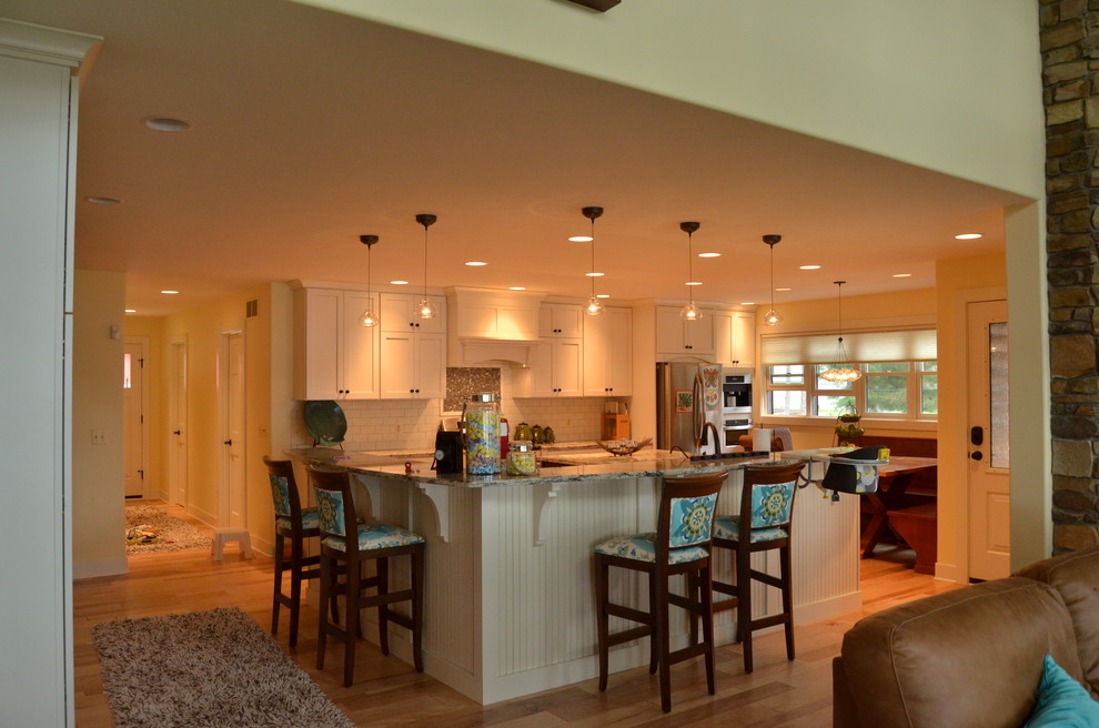 This is an example of an expansive eclectic u-shaped open plan kitchen in Grand Rapids with an undermount sink, recessed-panel cabinets, light wood cabinets, solid surface benchtops, white splashback, subway tile splashback, stainless steel appliances, medium hardwood floors and with island.