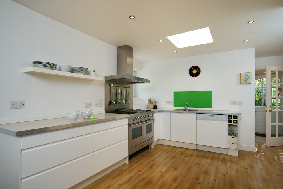 Design ideas for a large contemporary l-shaped eat-in kitchen in Other with flat-panel cabinets, green splashback, glass sheet splashback, stainless steel appliances, white cabinets, a single-bowl sink, laminate benchtops, light hardwood floors and no island.