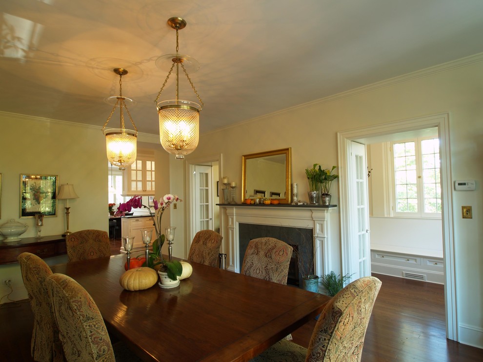 This is an example of a mid-sized traditional separate dining room in New York with white walls, dark hardwood floors, a two-sided fireplace, a stone fireplace surround and brown floor.