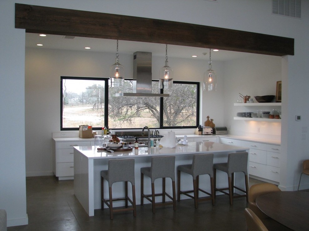 Mid-sized transitional l-shaped concrete floor eat-in kitchen photo in Austin with an undermount sink, flat-panel cabinets, white cabinets, solid surface countertops, stainless steel appliances and an island