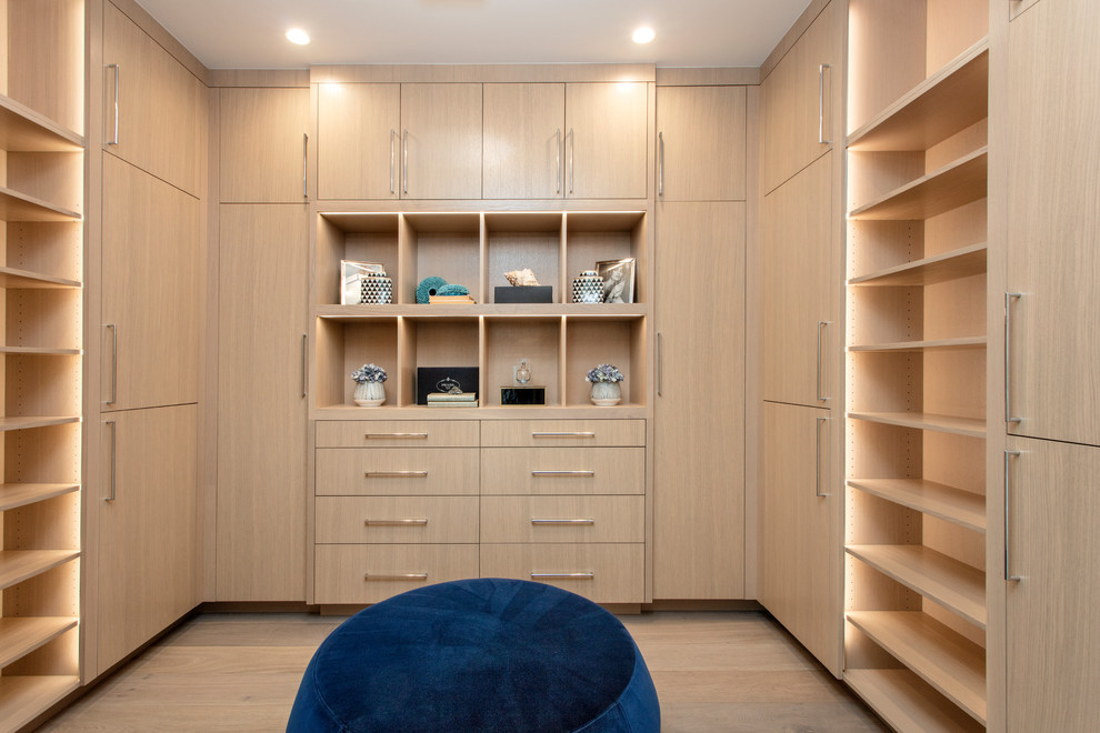 Large beach style gender-neutral walk-in wardrobe in Orange County with flat-panel cabinets, light wood cabinets, light hardwood floors and beige floor.