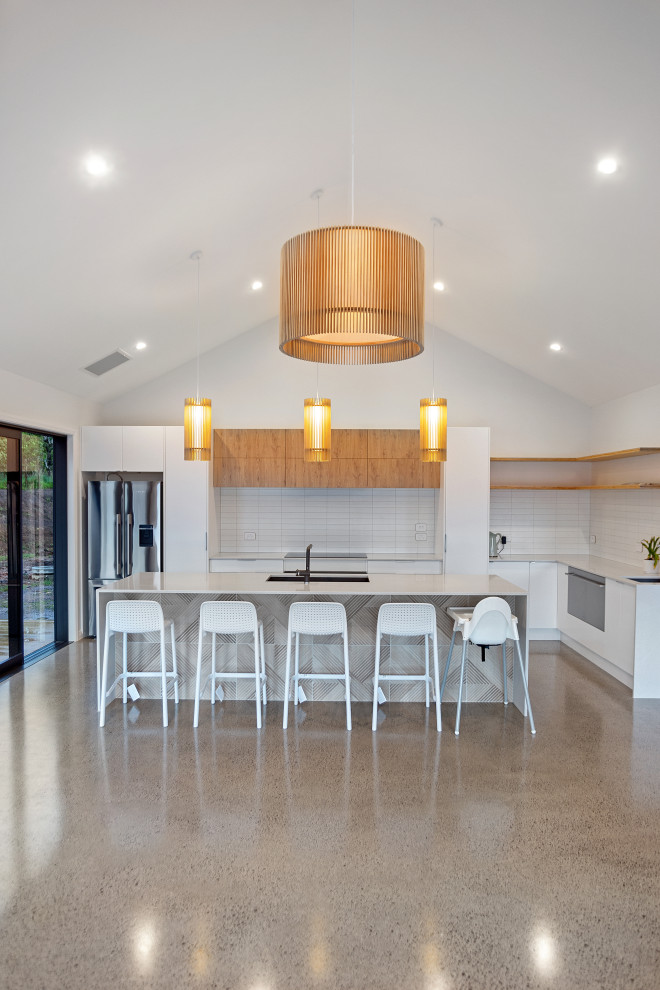 Ejemplo de cocina moderna de tamaño medio con salpicadero blanco, electrodomésticos de acero inoxidable, suelo de cemento y una isla