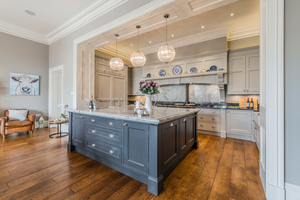 Photo of a large country u-shaped open plan kitchen in Cheshire with medium hardwood floors, with island, recessed-panel cabinets, grey cabinets, grey splashback, stone slab splashback and brown floor.