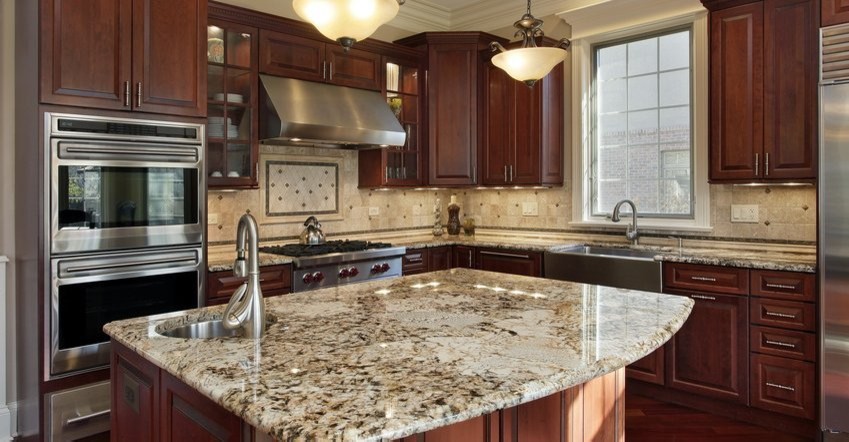 Example of a large trendy l-shaped dark wood floor enclosed kitchen design with a farmhouse sink, raised-panel cabinets, dark wood cabinets, granite countertops, beige backsplash, stone tile backsplash, stainless steel appliances and an island